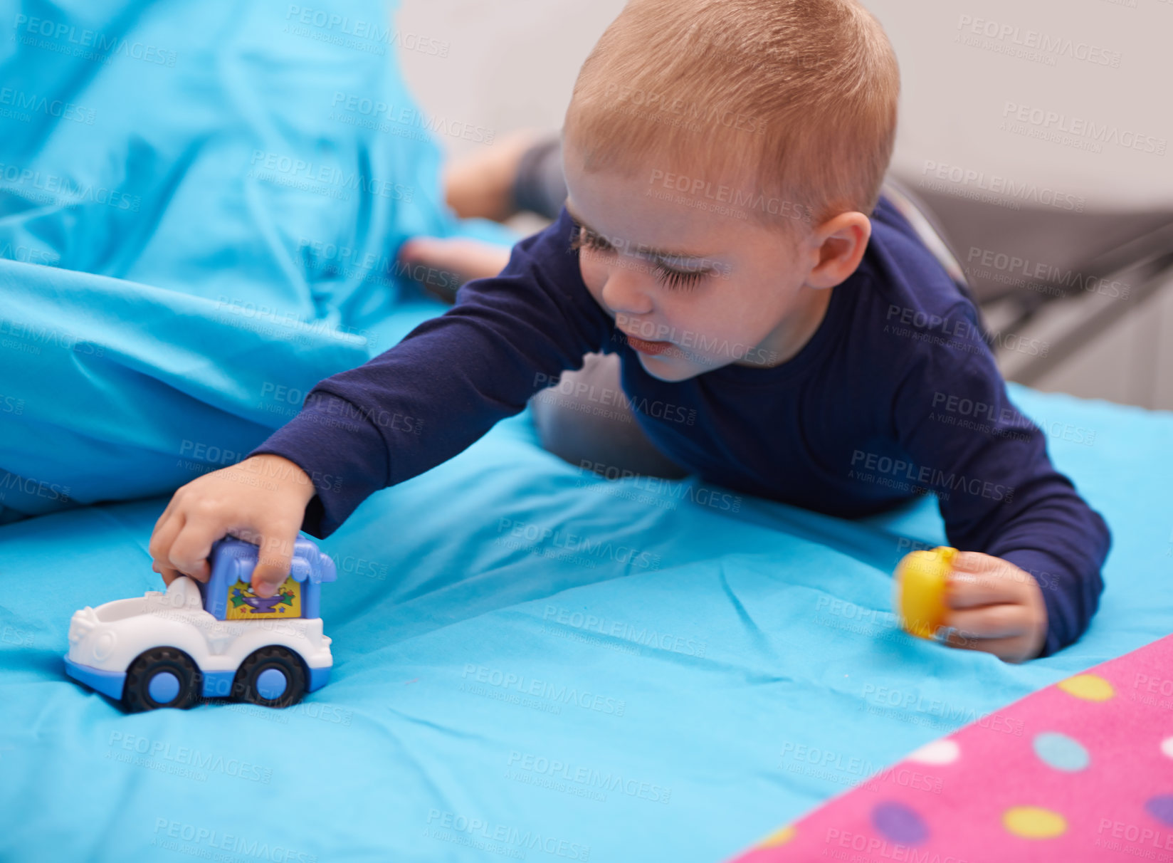 Buy stock photo A little boy playing with a toy car on his bed