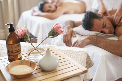 Buy stock photo Hotel, flowers and couple in spa to relax on bed or break with luxury pamper treatment tools on table. Protea, facial oil or woman with man at resort or salon for natural healing benefits or massage