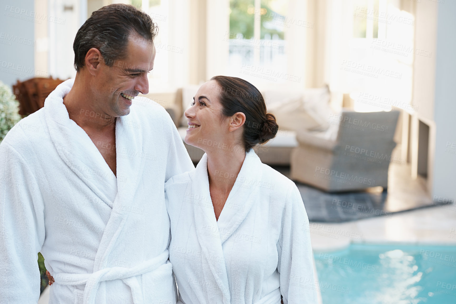 Buy stock photo Holiday, robe and couple at hotel pool with smile, embrace and relax together at wellness spa getaway. Hospitality, happy woman and man at luxury villa for travel, vacation and love on romantic date