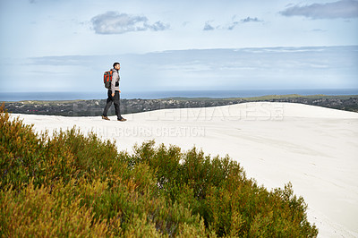 Buy stock photo Shot of a young male hiker walking along the sand dunes