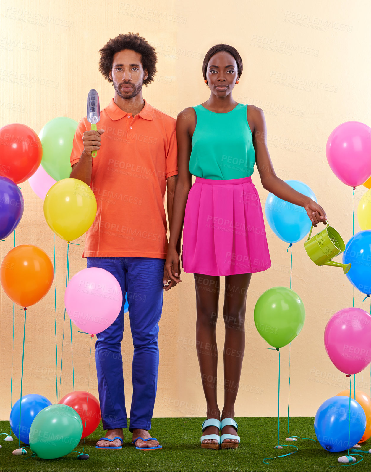 Buy stock photo An awkward african couple surround by colorful balloons while holding hands