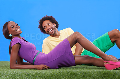 Buy stock photo Black couple, laughing and lying with fashion on grass for funny joke, meme or colorful style on a blue studio background. Young African man and woman with smile in stylish clothing on mockup space