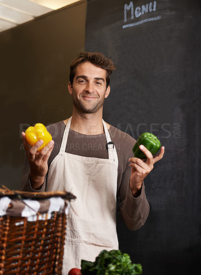 Buy stock photo A young man holding a yellow and green pepper in a kitchen