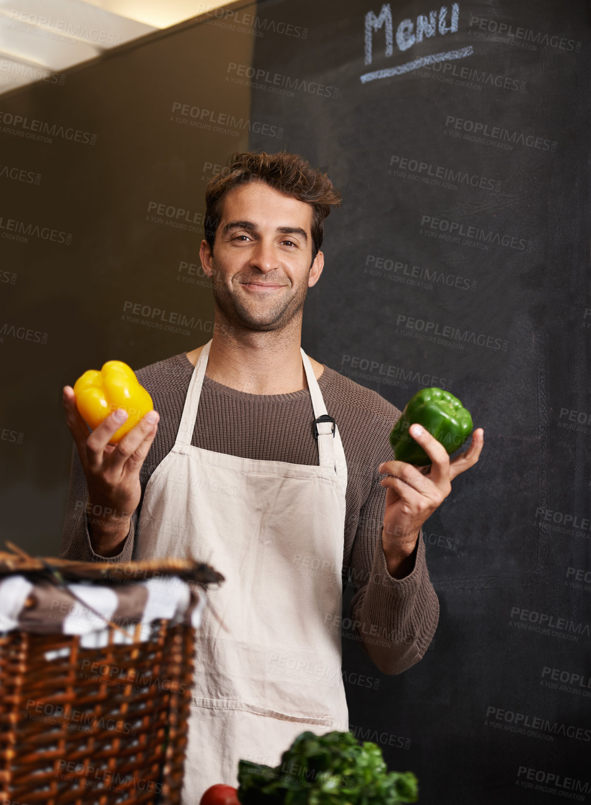Buy stock photo A young man holding a yellow and green pepper in a kitchen
