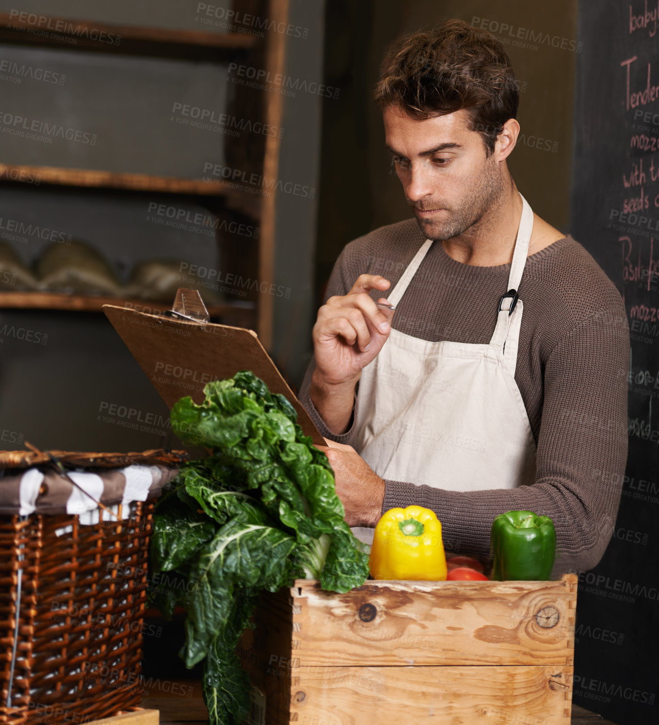 Buy stock photo A young man with a clipboard standing beside a crate full of vegetables