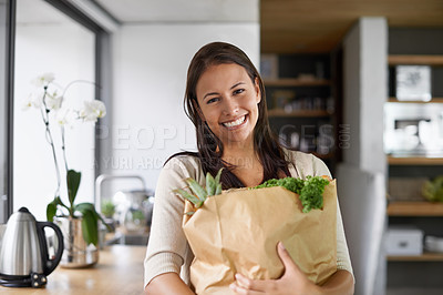 Buy stock photo A young woman standing in her kitchen holding a bag of groceries - portrait