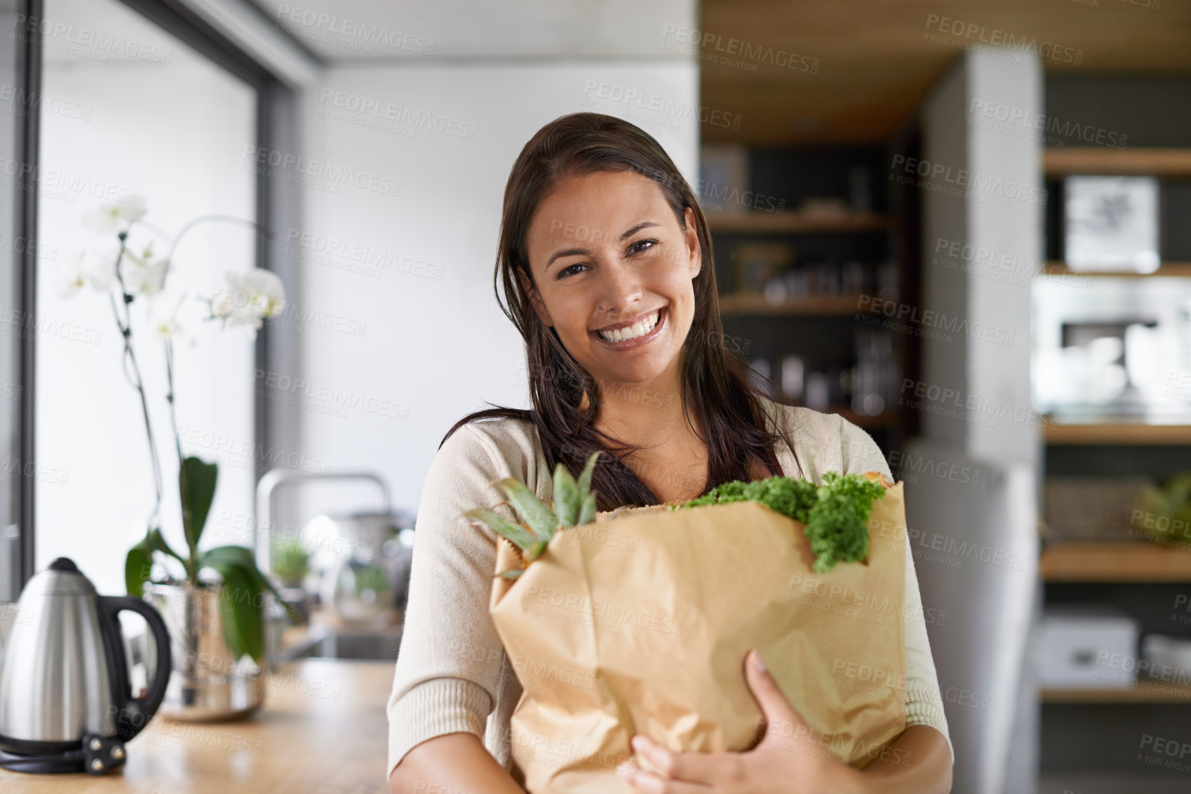 Buy stock photo A young woman standing in her kitchen holding a bag of groceries - portrait