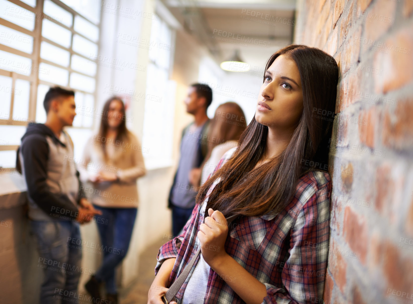 Buy stock photo Shot of a beautiful young female student looking bored while leaning against a brick wall on campus