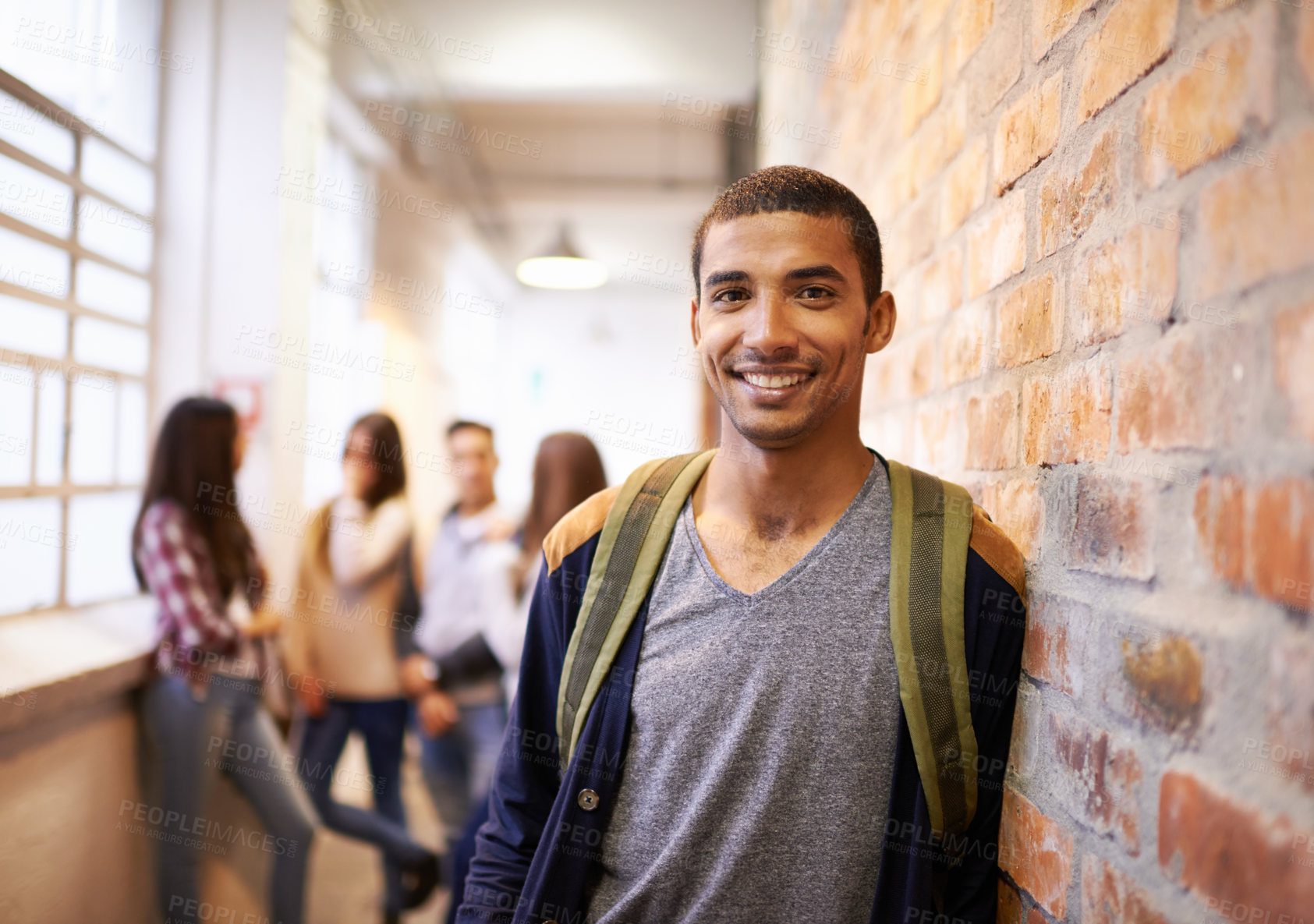 Buy stock photo Portrait of a handsome young male student leaning against a wall with his friends in the background