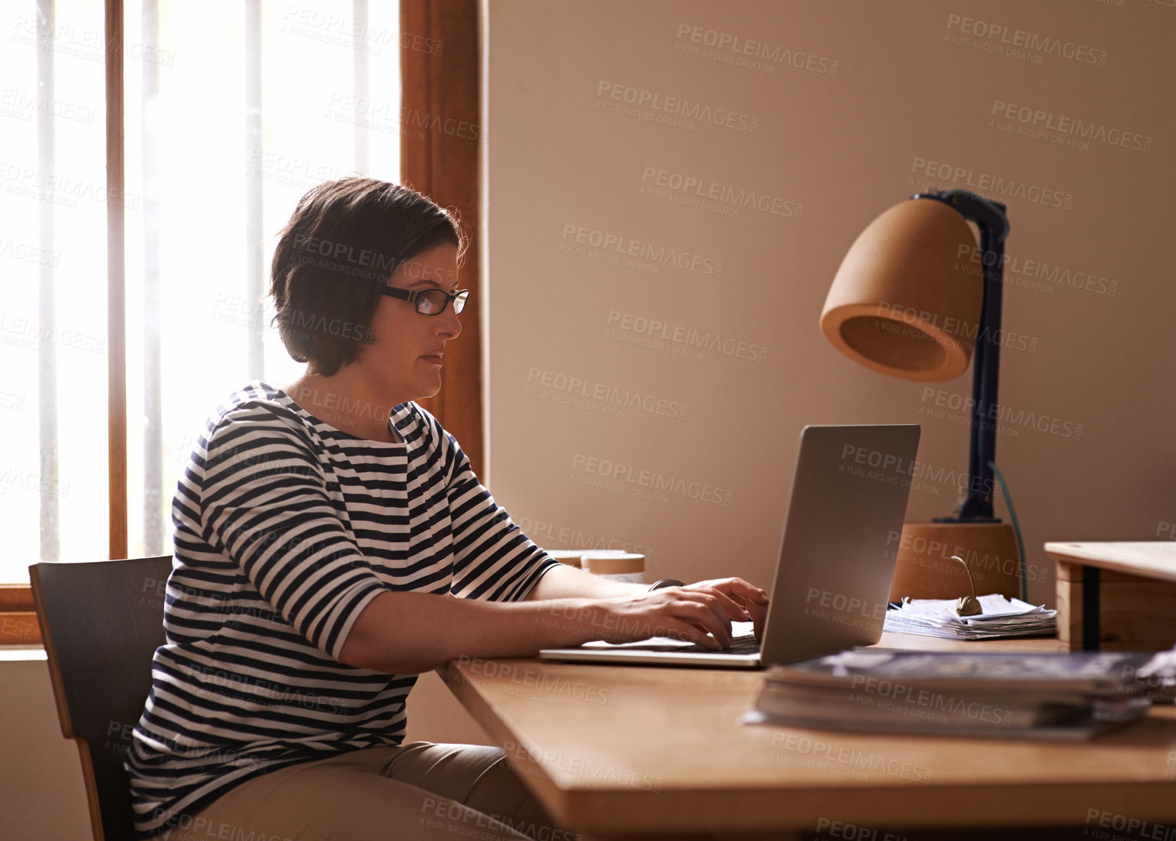 Buy stock photo A cropped shot of a woman sitting at a desk in her home and working on a laptop