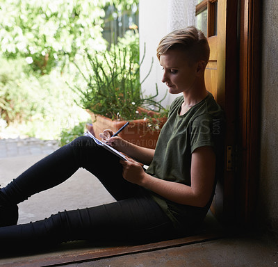 Buy stock photo Shot of an attractive young woman sitting outside on the porch writing in a notepad