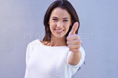Buy stock photo Portrait of a happy young woman standing against a gray background and giving thumbs up