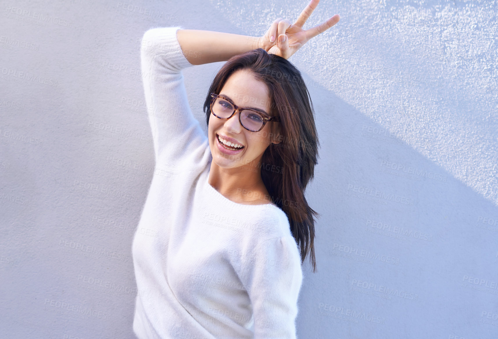 Buy stock photo Portrait, fashion and happy with bunny ears woman on wall background for comedy, fun or humor. Smile, glasses and hand gesture with confident young person in trendy or casual clothing outfit