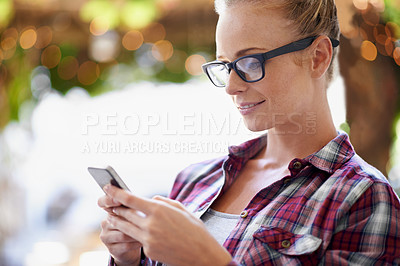 Buy stock photo A cropped shot of a beautiful young woman sitting outdoors and using her mobile phone