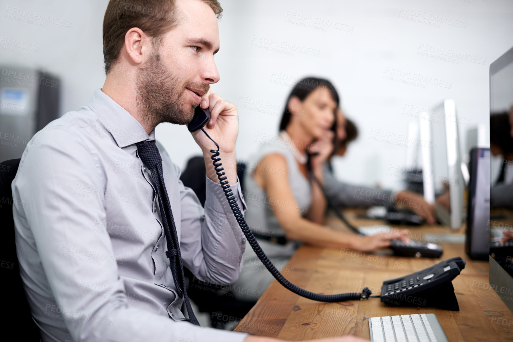 Buy stock photo Shot of a man taking a call in an office with his colleagues in the background