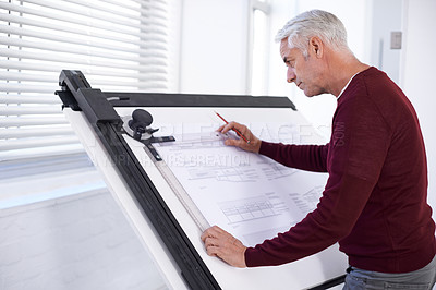 Buy stock photo Cropped shot of a male architect working on a building plan at a drawing board