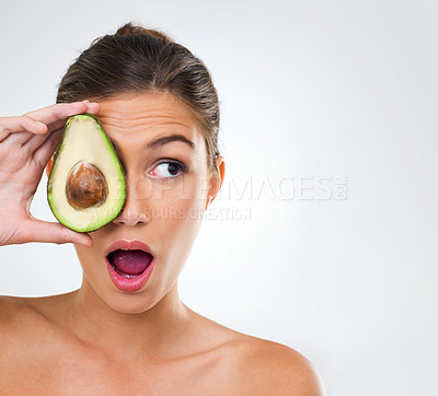 Buy stock photo Shot of a gorgeous young woman holding half an avocado over the side of her face