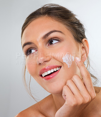 Buy stock photo Cropped studio shot of a beautiful young woman applying cream to her face