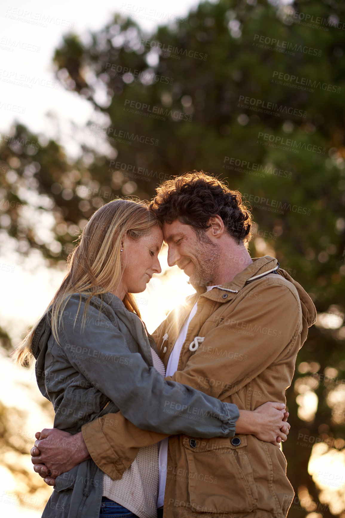 Buy stock photo Outdoor, hug and couple with love, sunshine and happiness with romance and cheerful in a park. People, embrace and woman with man or date with marriage or relationship with sunset or bonding together