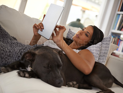 Buy stock photo Shot of an attractive young woman relaxing on the sofa with her dog and using a digital tablet