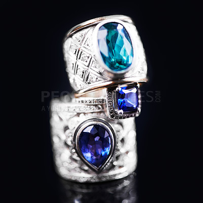 Buy stock photo Gemstone, silver and rings on a black background of luxury or expensive present for engagement or marriage in studio. Jewelry, diamonds and blue or sapphire rock in closeup, stack and rich accessory