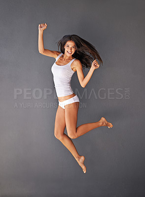Buy stock photo Full-length shot of a healthy young woman jumping against a gray background