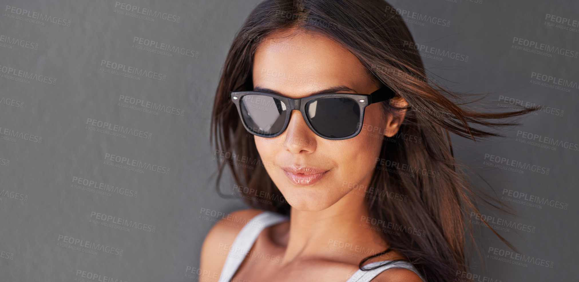 Buy stock photo Beautiful, attractive and trendy portrait of a young woman isolated against a grey wall. Stylish, sexy and funky girl wearing sunglasses against a copy space background with a cool facial attitude 