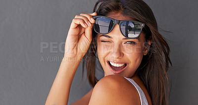 Buy stock photo Shot of an attractive young woman winking at the camera while holding up her sunglasses