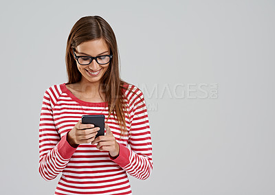 Buy stock photo Studio shot of an attractive young woman using a smartphone on a grey background