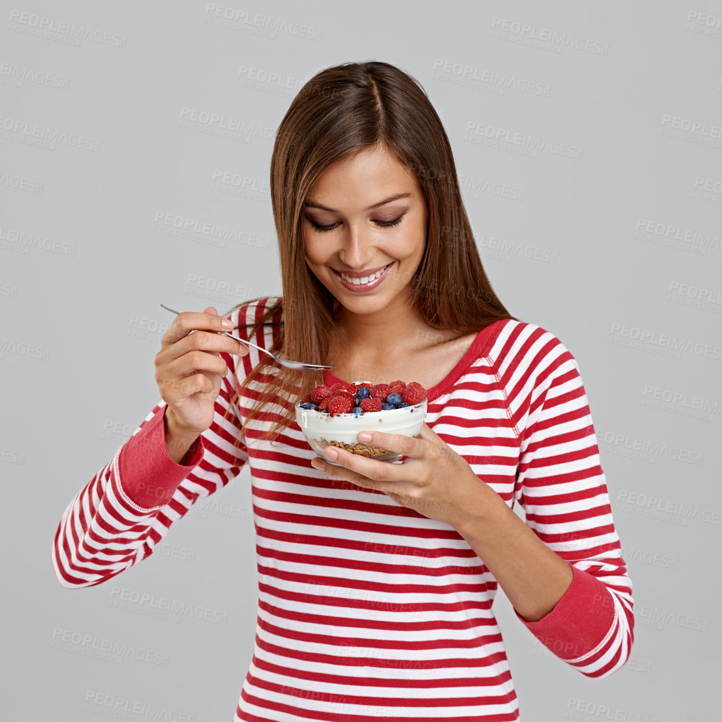 Buy stock photo Studio shot of an attractive young woman eating a bowl of berries on a grey background