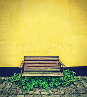 Buy stock photo Wooden bench, yellow wall background and plants with stones, outdoor and environment with garden furniture. Outdoor, seating and chair with growth and fresh air with cobblestone, bushes and street