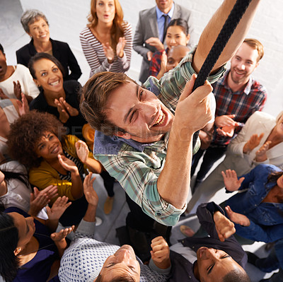 Buy stock photo Business people, smile and man climbing rope for goals, target or achievement with team support. High angle, diversity and happy professional person with group of colleagues for ambition in office.