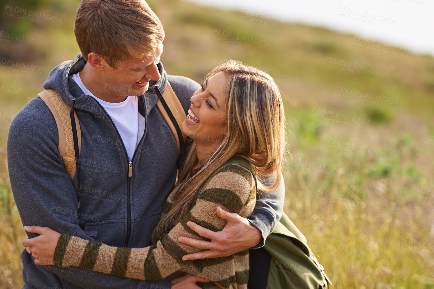 Buy stock photo Happy, love and funny couple hug in nature for hiking, bonding or fun with joke, humor or comic. Laugh, eye contact or people embrace on countryside field on adventure, journey or trekking travel