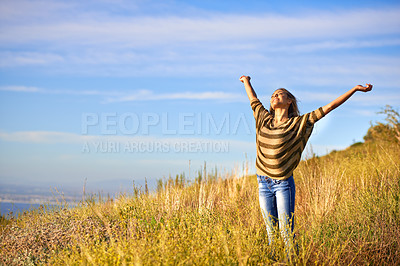 Buy stock photo Shot of an attractive young woman standing in a field on a hillside with her arms in the air