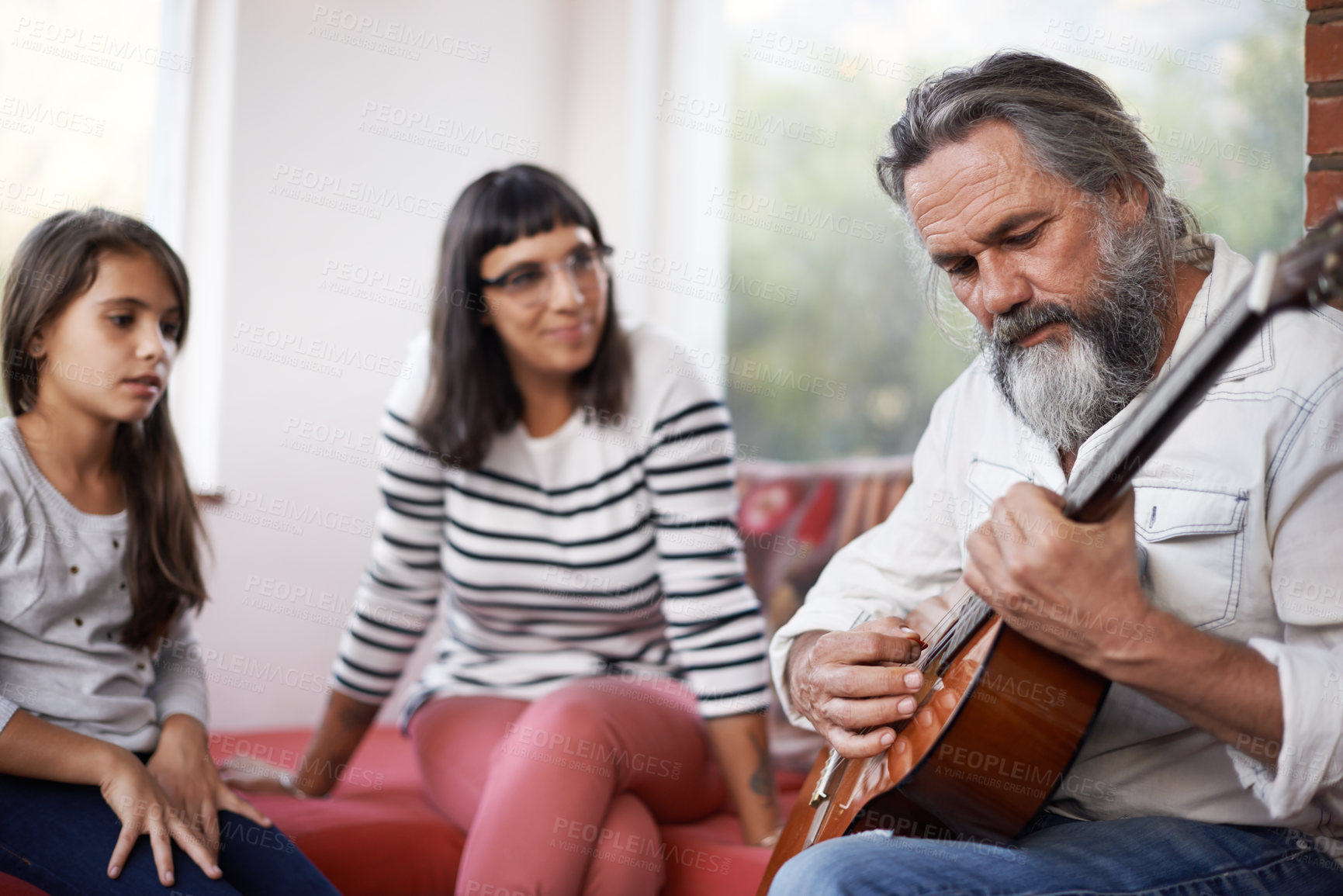 Buy stock photo Shot of a senior man playing the guitar while sitting with his family