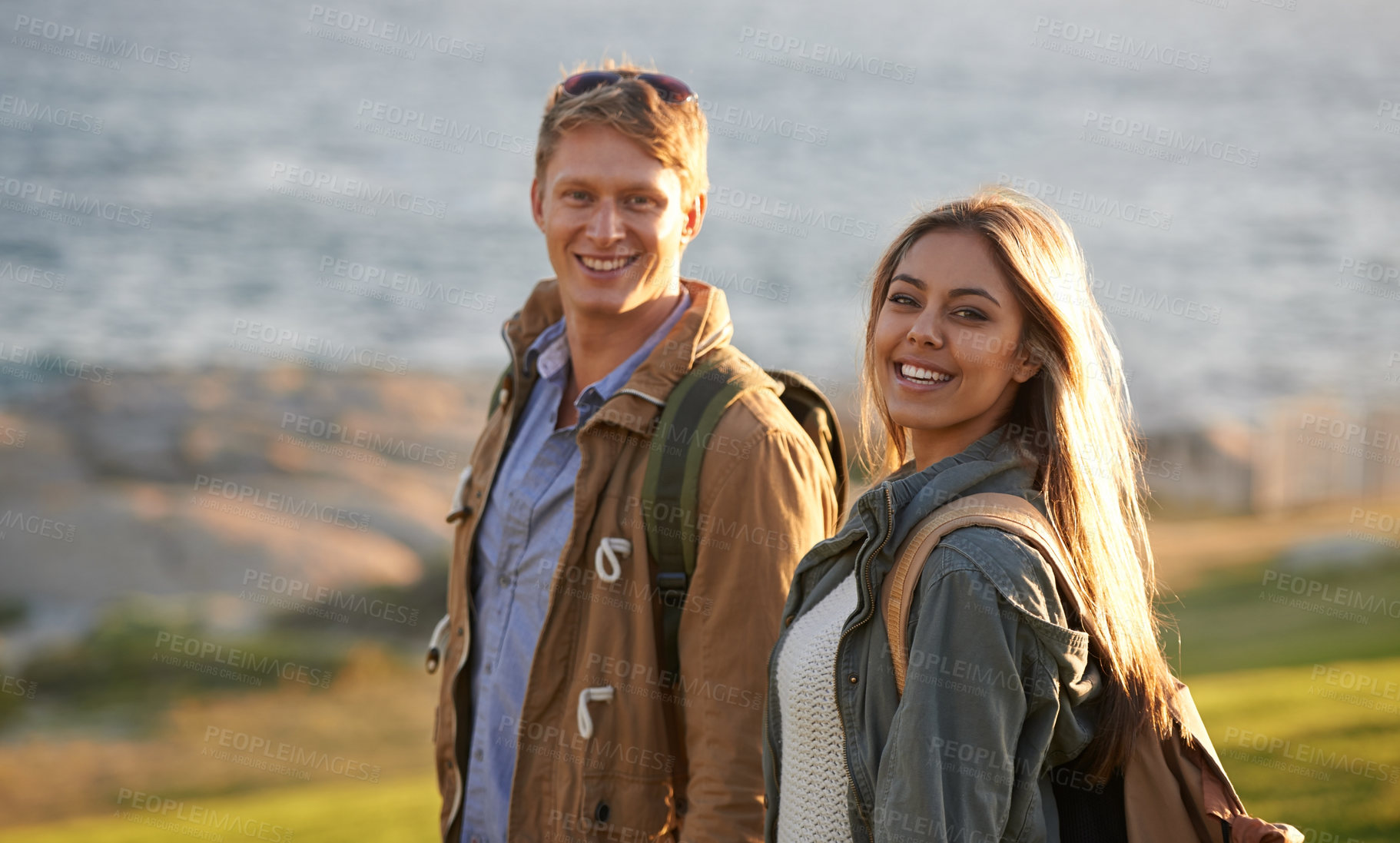 Buy stock photo Love, portrait and happy couple on hike with ocean, sunset for tropical holiday adventure, relax and bonding together. Smile, man and woman on romantic date with beach, nature and grass on vacation