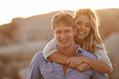 Buy stock photo A happy young couple enjoying a piggyback ride on the beach at sunset