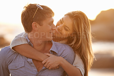 Buy stock photo Shot of a happy young couple enjoying a piggyback ride on the beach at sunset