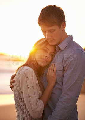 Buy stock photo Portrait of a happy young couple enjoying a romantic embrace on the beach at sunset