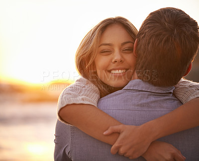 Buy stock photo Portrait of a happy young couple enjoying a romantic embrace on the beach at sunset