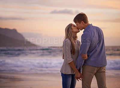 Buy stock photo Shot of a young couple enjoying a romantic kiss on the beach at sunset