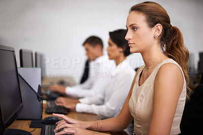 Buy stock photo Shot of an attractive young office worker at her computer with her colleagues in the background