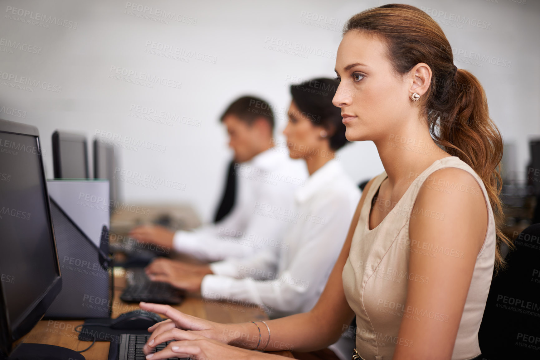 Buy stock photo Shot of an attractive young office worker at her computer with her colleagues in the background