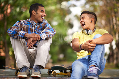 Buy stock photo Shot of two young men having a laugh while out skateboarding