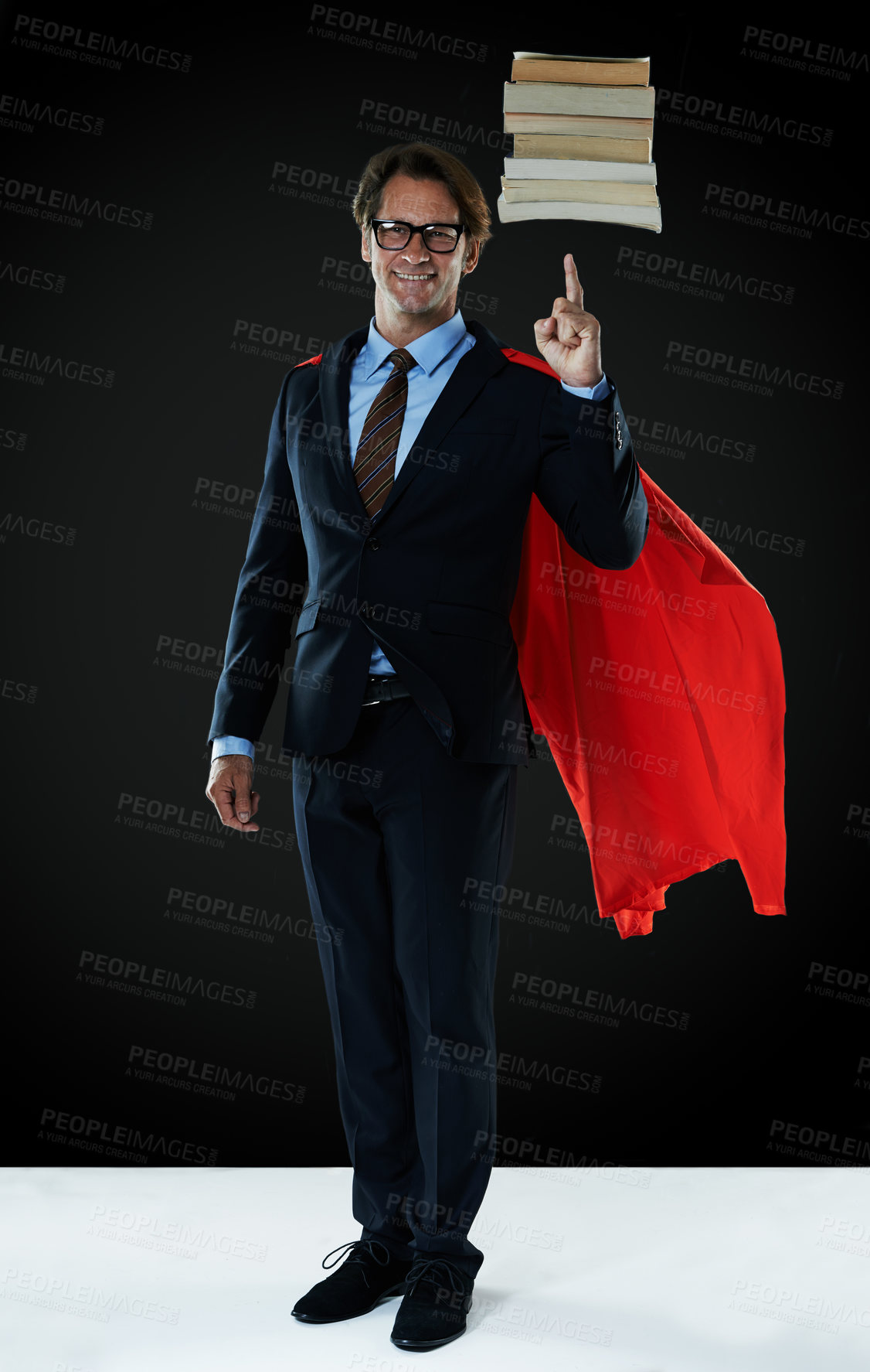 Buy stock photo Shot of a businessman  wearing a red cape hovering books over his finger
