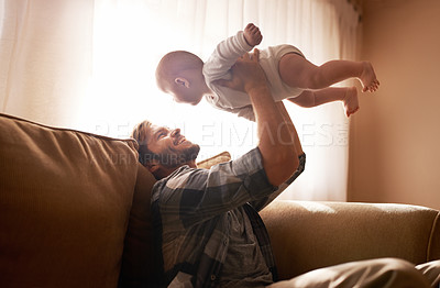 Buy stock photo Dad, funny and lifting baby on sofa in home living room, playing or bonding together. Laughing, care and father holding infant, newborn or child on couch in lounge, having fun and enjoying time.