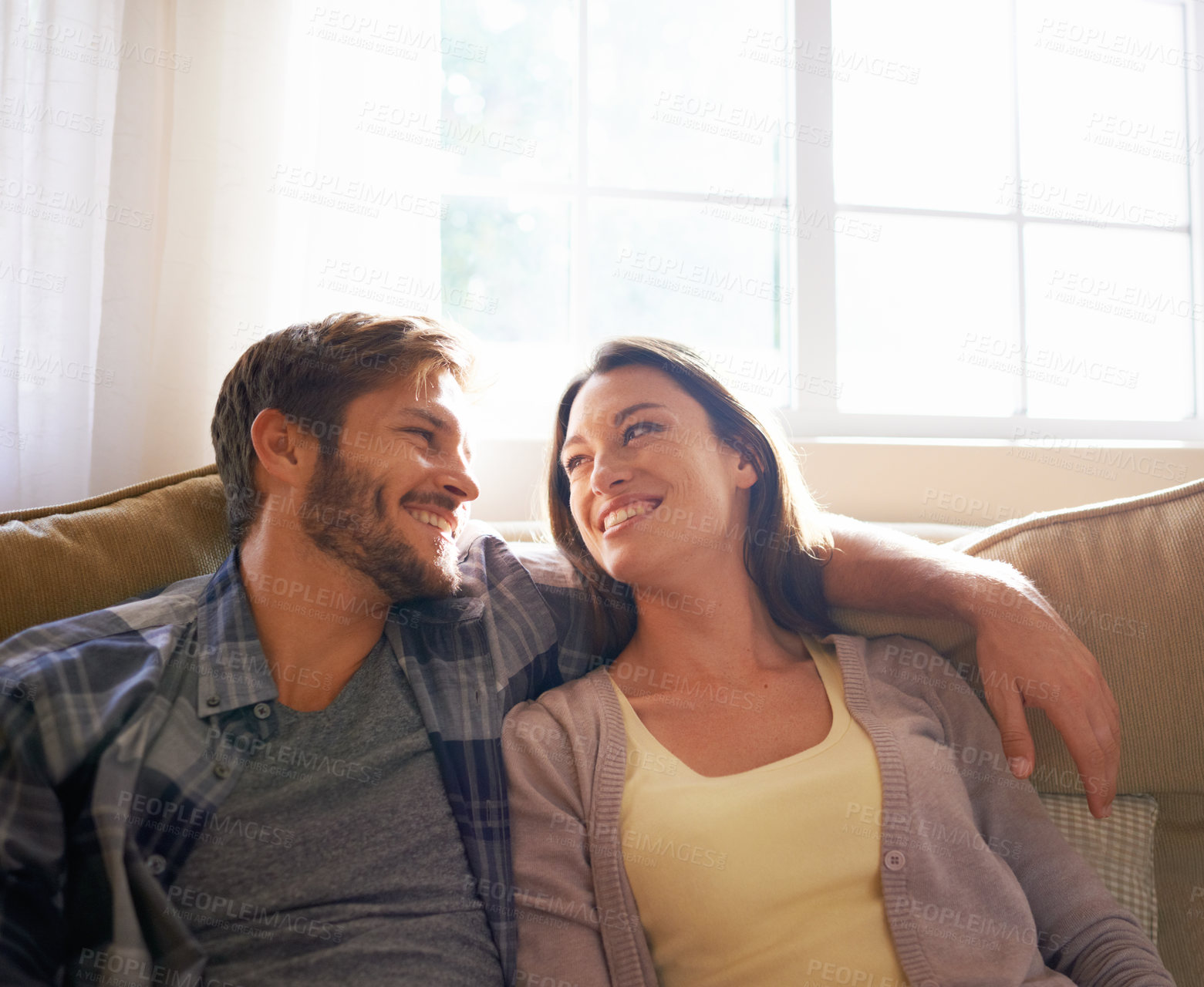 Buy stock photo Couple, love and hug or smile at each other on a couch or in the living room and conversation. Man, woman and relationship or bonding and happy partners affectionate or at home relaxing and embrace