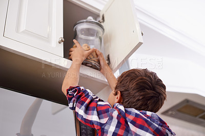 Buy stock photo Kitchen, cupboard and cookie jar with boy child reaching for treats for hunger in home from below. Biscuits, food or snack in glass with young kid in apartment, stealing baked goods to eat from back