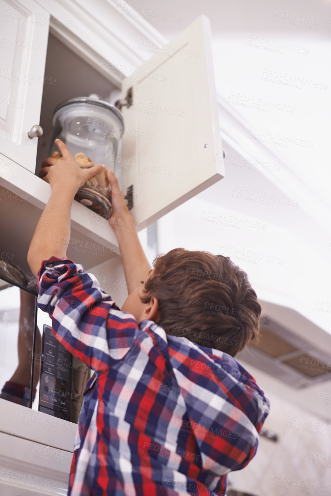 Buy stock photo A young boy reaching for a cookie jar in the top kitchen cupboard