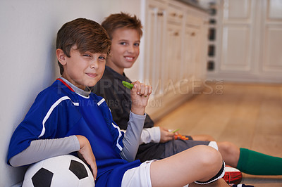Buy stock photo Shot of two little boys sitting with a soccer ball and having healthy snacks